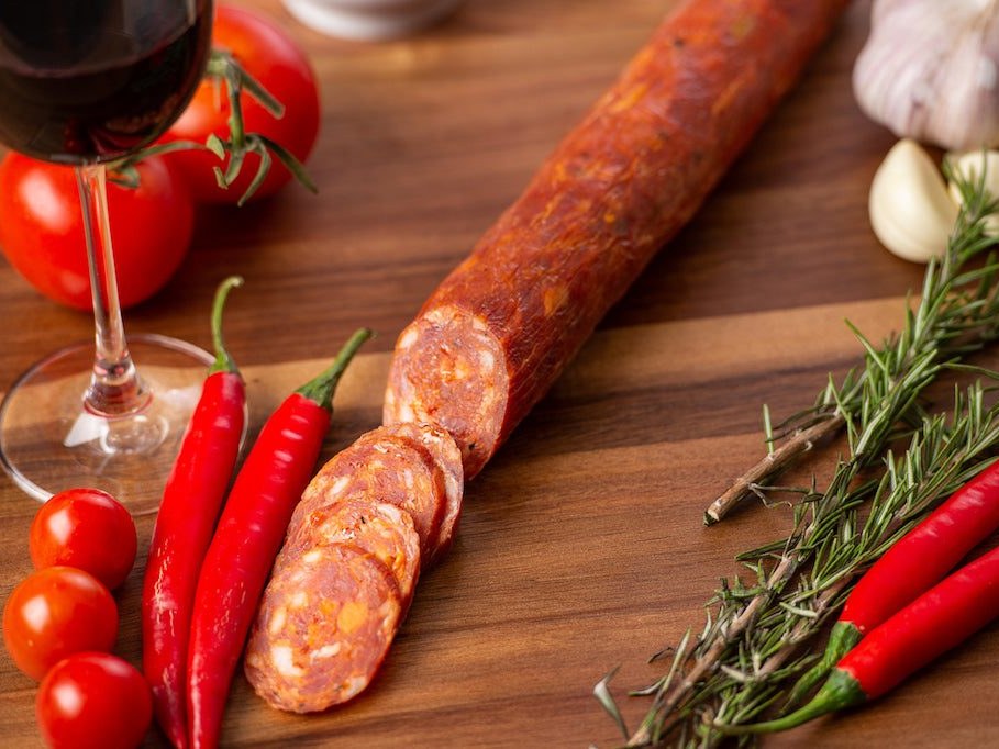 Sliced pepperoni salami with red wine, chillies and tomatoes on a timber board