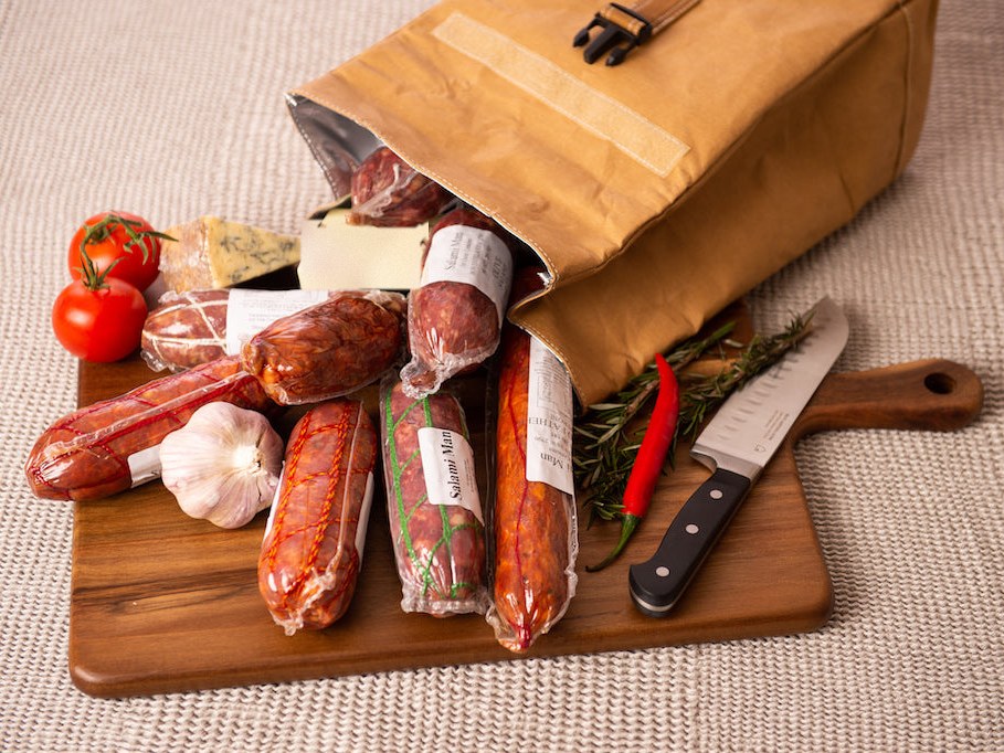Whole salami sticks tumbling from a canvas bag onto a timber board