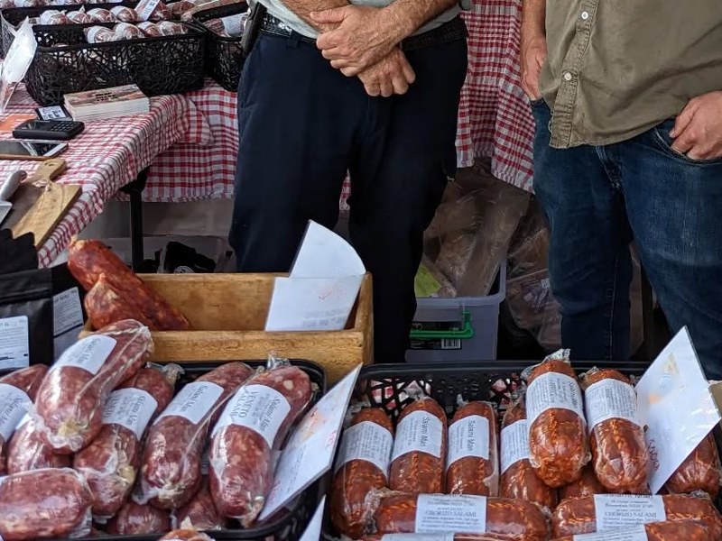 Salami Man market stall with whole salami in baskets on a checked tablecloth