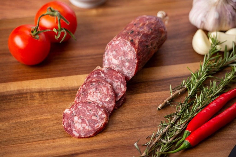 Sliced salami with rosemary, chillies and tomatoes on a timber board