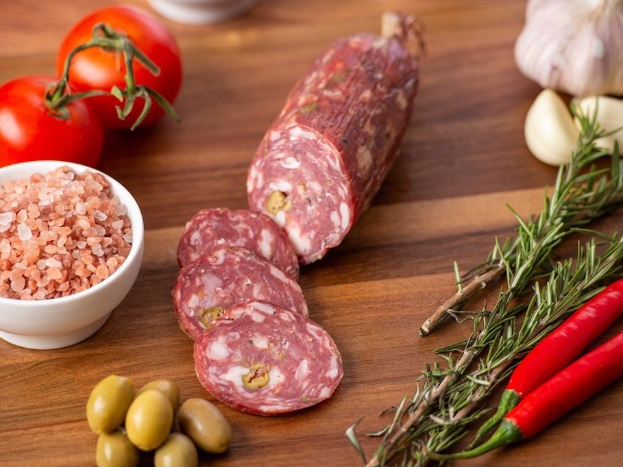 Sliced salami with green olives, pink salt and rosemary on a timber board