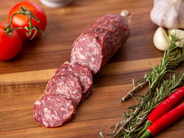 Sliced salami on a timber board with tomatoes, garlic, rosemary and chillies