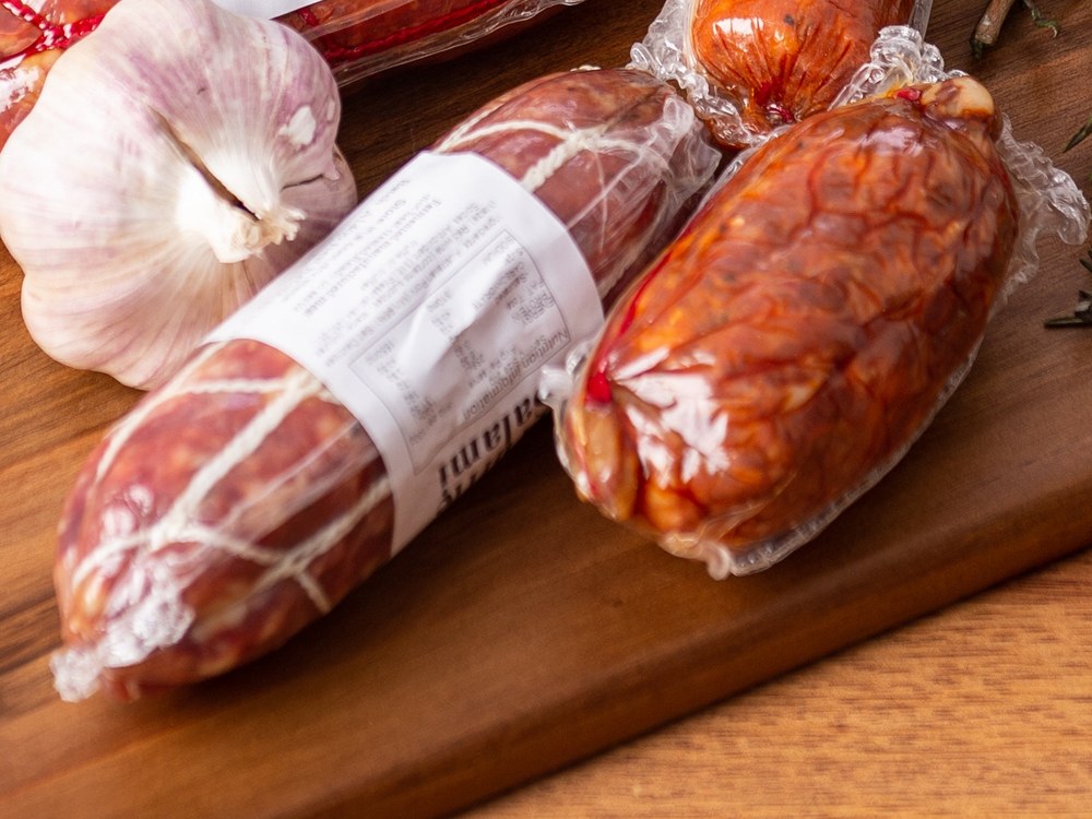 Vacuum packed salami sticks and a garlic bulb on a timber board